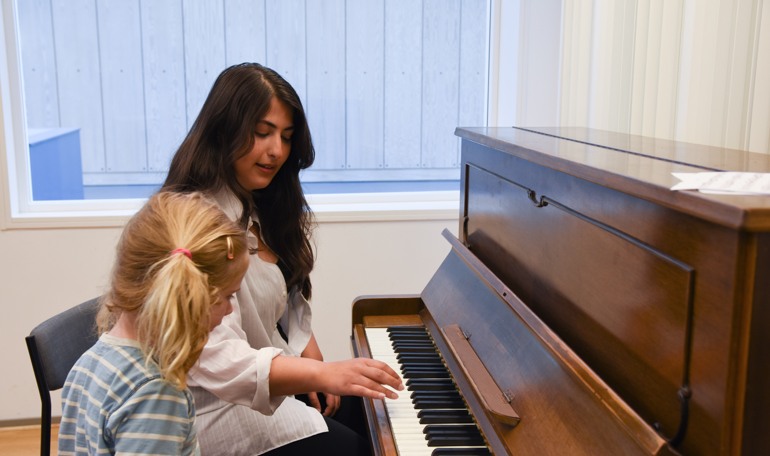 Kvinna visar barn hur barnet ska hålla fingrarna på pianots tangenter